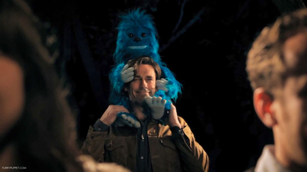 Jon Hamm die een blauwe yeti handpop een piggyback geeft