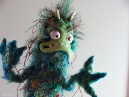 Títere monstruo inspirado en una bacteria, con expresión salvaje y pelaje verde.