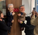 Likeness puppets of Anderson Cooper and Andy Cohen in CNN office, pointing at the CNN logo on a door.