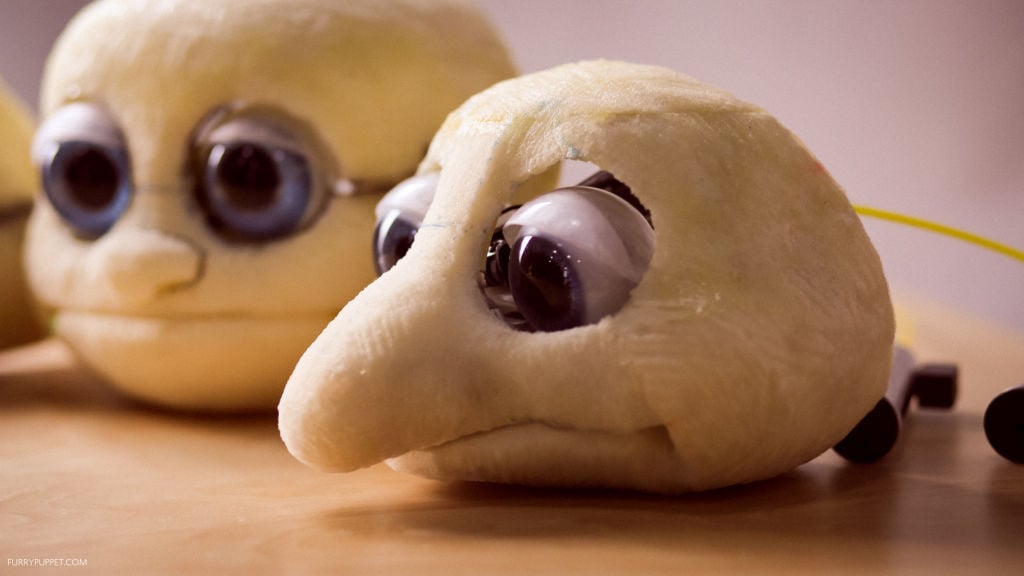 Bare foam head with mechanical eyelids over glass wide, on puppet builder's desk