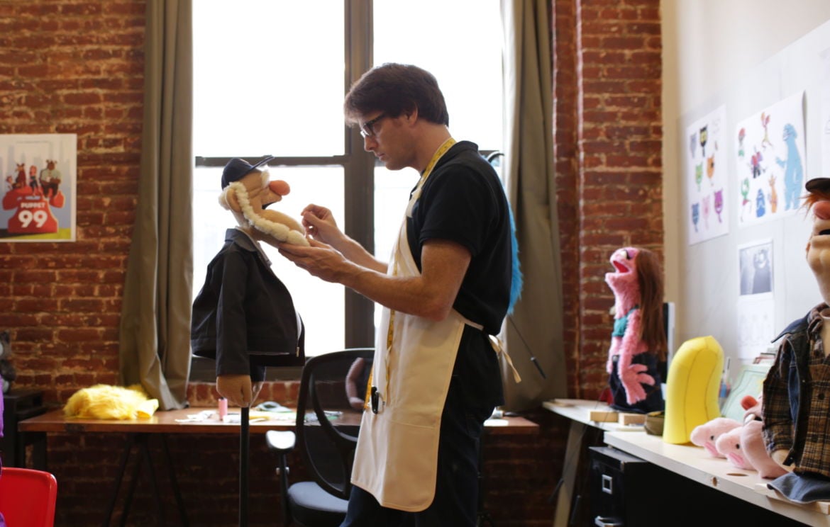 Un artista al lavoro in uno studio di burattini a New York. Burattini a mano assortiti sullo sfondo.